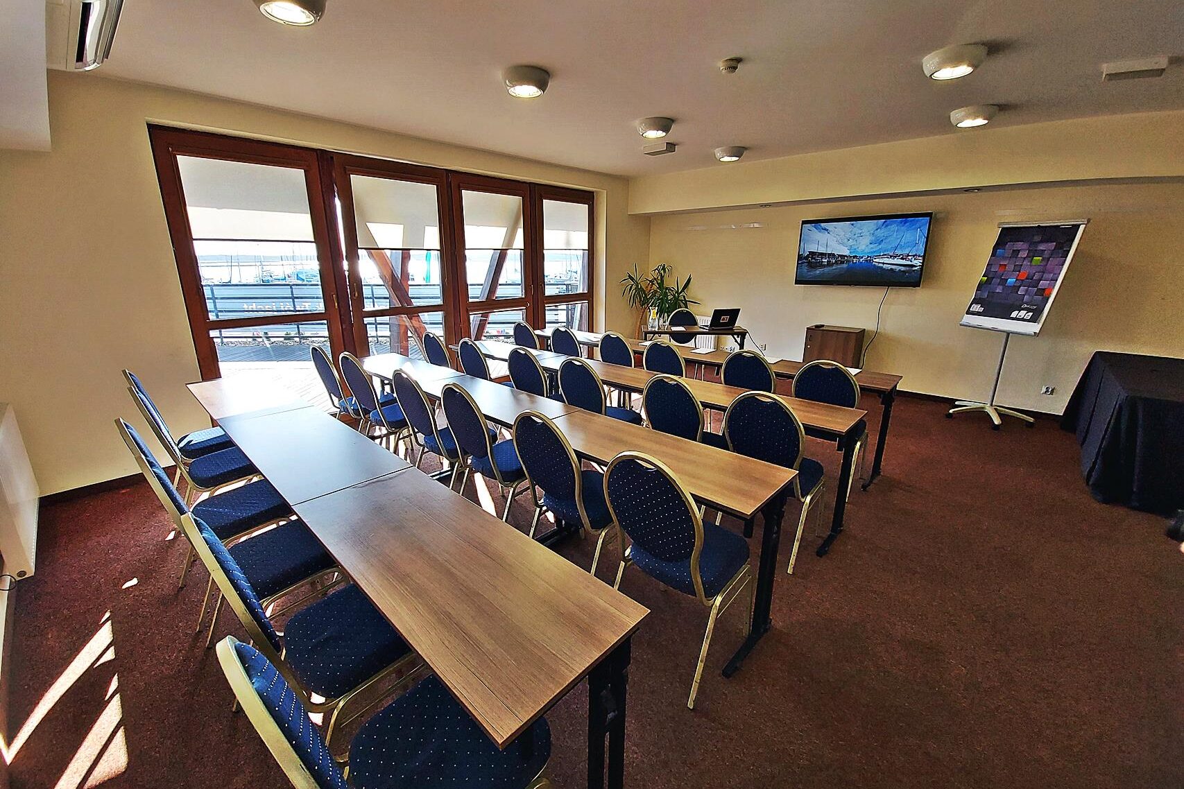 Sala konferencyjna Hotelu Galion ze stołami ustawionymi w podkowę, krzesłami i ekranem.
